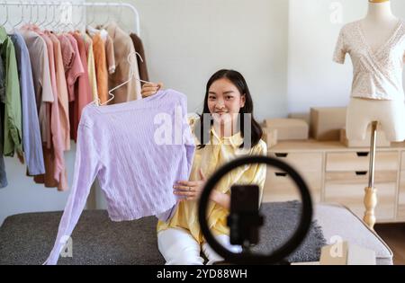 Giovane ragazza asiatica consultazione online con stilista designer prendere online video corso o formazione di vestiti eleganti su appendiabiti donna asiatica dre Foto Stock