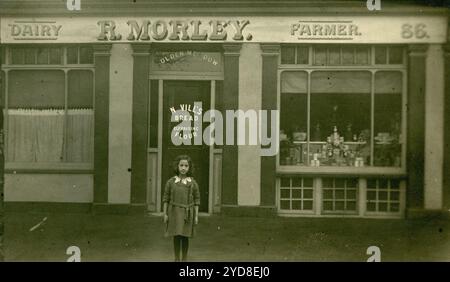 Cartolina originale dell'era della prima Guerra Mondiale di una bambina in piedi fuori in un negozio. R Morley, Dairy Farmer e' il segno del negozio. I locali del negozio di prodotti caseari erano al 86 di Richmond Road, Kingston, Surrey. Il cartello della vetrina pubblicizza il pane di Nevill. Circa 1913, Regno Unito Foto Stock