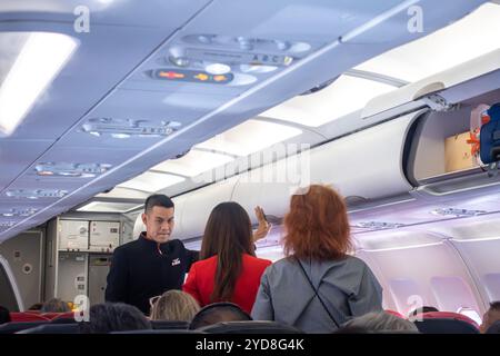 Assistenti di volo, uomini e donne, uomini e donne in uniforme che assistono i passeggeri nella preparazione del volo Airbus A320 con AirAsia Indonesia Foto Stock