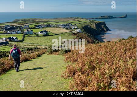 Uomo che cammina sul sentiero e ammira Rhossili e Worms Head da Rhossili Down, Gower, Galles, Regno Unito Foto Stock