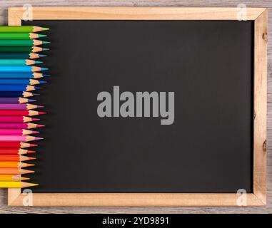 Le matite dai colori nitidi sono disposte in modo ordinato su una lavagna nera con spazio per le copie. Primo piano: Scuola - cancelleria. Foto Stock