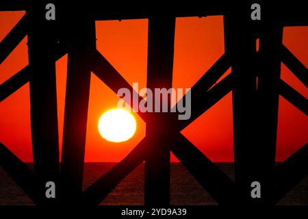 Isola di Palms, Stati Uniti. 24 ottobre 2024. Il gigantesco sole arancione sorge sull'Oceano Atlantico visto attraverso i supporti del molo dell'Isola di Palms a Front Beach, il 24 ottobre 2024 a Isle of Palms, Carolina del Sud. Il clima caldo e soleggiato è previsto per le prossime settimane per il basso paese. Crediti: Richard Ellis/Richard Ellis/Alamy Live News Foto Stock