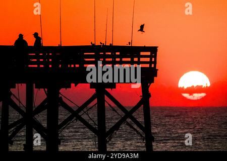 Isola di Palms, Stati Uniti. 25 ottobre 2024. I pescatori fiancheggiati dall'alba, chiacchierano mentre il gigantesco sole arancione sorge sull'Oceano Atlantico al molo Isle of Palms di Front Beach, il 25 ottobre 2024 a Isle of Palms, South Carolina. Il clima caldo e soleggiato è previsto per le prossime settimane per il basso paese. Crediti: Richard Ellis/Richard Ellis/Alamy Live News Foto Stock