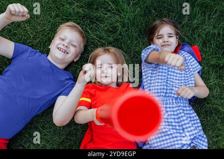 I bambini giacciono e ridono sul prato verde. I bambini adorabili si divertono all'aperto nel prato. I piccoli amici in abiti casual si divertono insieme. Foto Stock