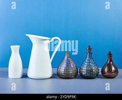 Set di vari flaconi, vasi e caraffe in vetro colorato e in metallo su sfondo blu. Foto Stock