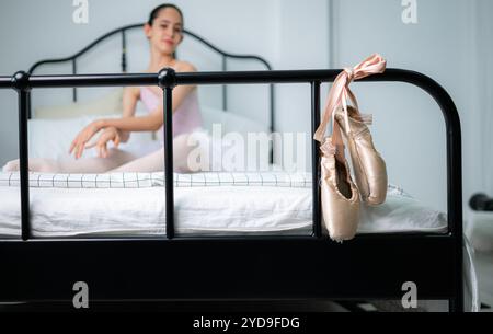 Una studentessa di balletto si riscalda a letto e guarda le vecchie scarpe da balletto appese alla fine del letto Foto Stock