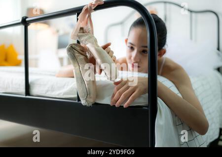 Una studentessa di danza femminile guarda le vecchie scarpe da balletto appese alla fine del letto, vuole cambiarsi in nuove scarpe da balletto. Foto Stock