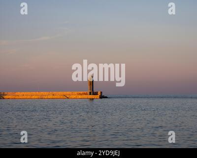 Breakwater con faro al tramonto. Acque calme dell'Adriatico. Sera. Foto Stock