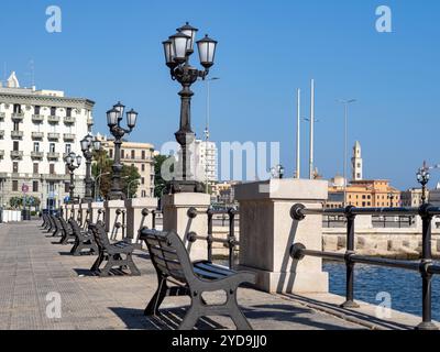 Lanterne e panchine sul lungomare di Bari, sullo sfondo l'edificio del teatro, estivo, soleggiato, senza persone. Foto Stock