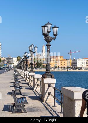 Lanterne e panchine sul lungomare di Bari, sullo sfondo l'edificio del teatro, estivo, soleggiato, senza persone. Foto Stock