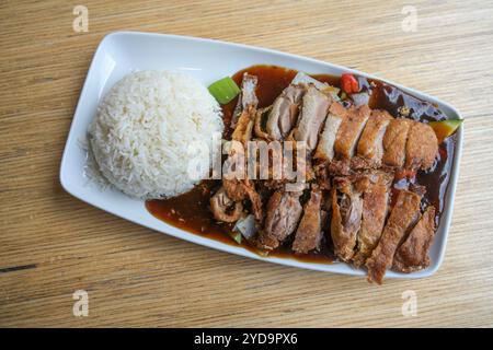 Croccanti fette di anatra arrosto sulle verdure con salsa e riso su un piatto quadrato bianco su un tavolo di legno in un ristorante cinese, vista dall'alto, c Foto Stock