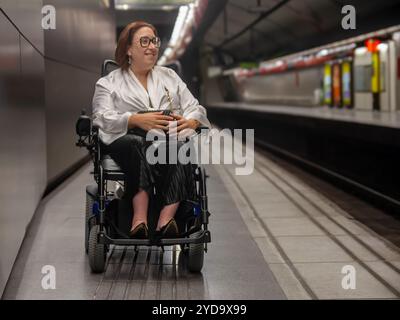 Donna in sedia a rotelle che aspetta sul binario della metropolitana per il treno Foto Stock