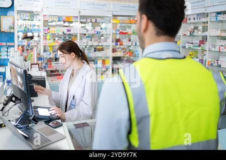 Il farmacista fornisce la medicina agli ingegneri che vengono a comprare la medicina in farmacia Foto Stock