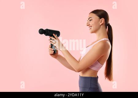 Giovane donna con massaggiatore percussivo su sfondo rosa Foto Stock