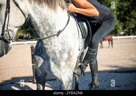 primo piano di una donna equestre non riconosciuta mentre si prepara a montare il suo cavallo, posizionando i suoi stivali sulla staffa. L'attenzione sui suoi stivali e sulla staffa Foto Stock