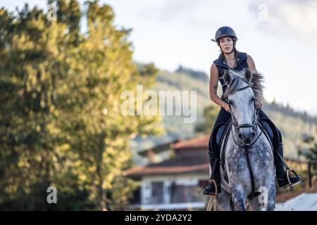 la giovane donna dinamica copyspace si dirige con sicurezza verso la telecamera sul suo cavallo durante l'allenamento presso il centro equestre. La scena cattura t Foto Stock