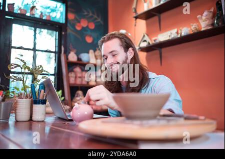 Un giovane uomo d'affari possiede una piccola azienda di ceramiche. Stanno costruendo se stessi risparmiando denaro per espandere la loro attività in futuro. Foto Stock