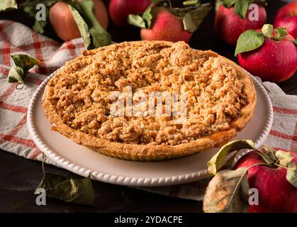 Primo piano di una torta di mele sbriciolata in un piatto bianco con mele appena raccolte Foto Stock