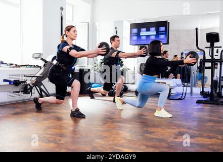 Coppia sportiva in tute ems allenata con personal trainer in palestra. Foto Stock