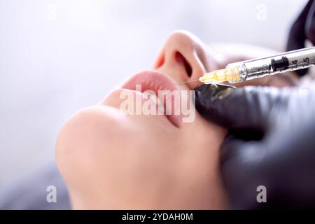 Iniezioni di bellezza. Cosmetologa donna in guanti neri fa un'iniezione Foto Stock