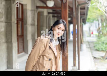 Una donna taiwanese dai capelli lunghi sui 20 anni che indossa un trench beige trascorre il pomeriggio invernale sotto le grondaie nel distretto di Xinyi, Taipei, Taiwan, ON Foto Stock