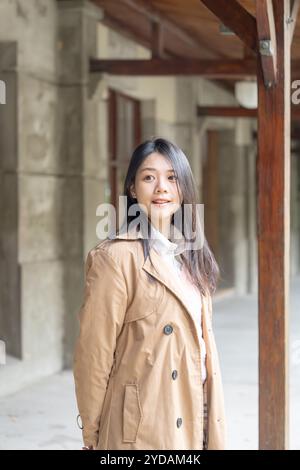 Una donna taiwanese dai capelli lunghi sui 20 anni che indossa un trench beige trascorre il pomeriggio invernale sotto le grondaie nel distretto di Xinyi, Taipei, Taiwan, ON Foto Stock
