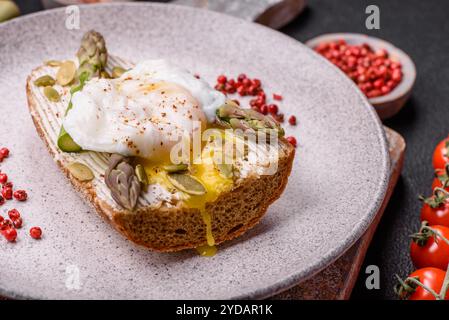 Colazione deliziosa e abbondante, con uova in camicia su pane tostato con formaggio spalmabile e asparagi Foto Stock