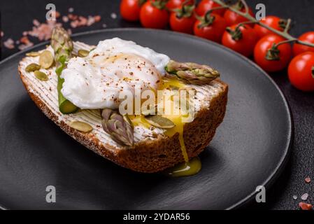 Colazione deliziosa e abbondante, con uova in camicia su pane tostato con formaggio spalmabile e asparagi Foto Stock