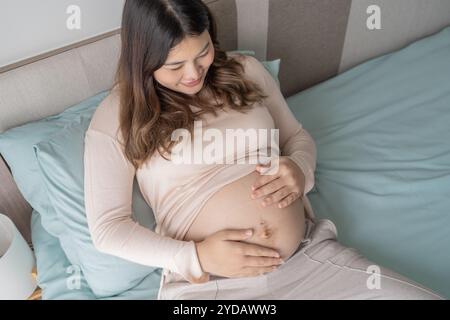 Donna asiatica incinta tiene le mani sulla pancia toccando il suo bambino curando la sua salute bella felice incinta womanÂ tenero umore Foto Stock