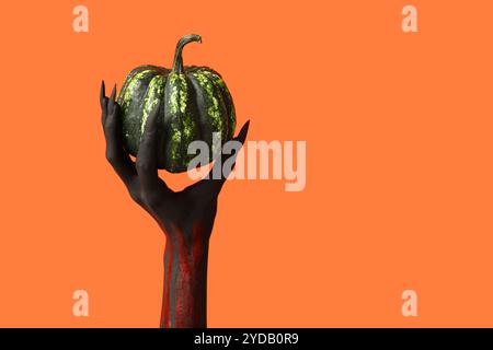 Mano di strega nera con artigli e zucca verde su sfondo arancione. Festa di Halloween Foto Stock