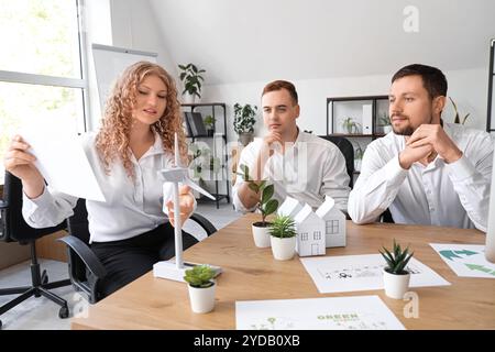 Colleghi con modelli di turbine eoliche e impianti sul tavolo durante una riunione di lavoro in ufficio. Concetto di energia verde Foto Stock