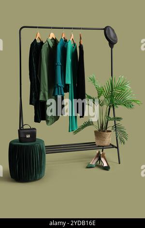 Scaffale con eleganti abiti femminili, accessori, scarpe e piante d'casa su sfondo verde Foto Stock