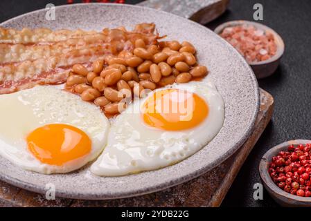 Colazione all'inglese con uova fritte, pancetta, fagioli, pomodori, spezie ed erbe aromatiche Foto Stock