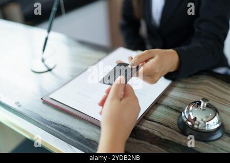 La receptionist dell'hotel in uniforme, il Concierge, dà la chiave che effettua il check-in al banco dell'hotel nella lobby, il personale è cordiale e accogliente nel conto della reception dell'hotel Foto Stock