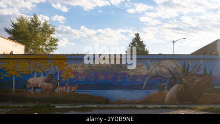 Murale dipinto a mano da Sophia Mathis a Townsend, Montana, con alci in una scena rurale con montagne, un lago e alberi di pioppo con fogliame autunnale. Foto Stock