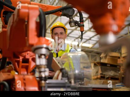 Un ingegnere maschio che controlla il funzionamento di un robot di saldatura. Utilizzato per il controllo di precisione della saldatura veloce ed estremamente sicuro Foto Stock