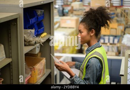 Lavoratrice di magazzino che conta gli articoli in un magazzino industriale al piano rialzato della fabbrica. che è uno spazio di archiviazione per piccole dimensioni Foto Stock