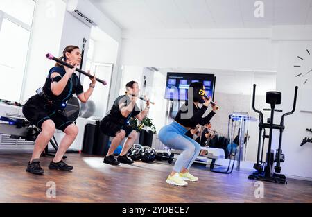 Coppia sportiva in tute ems con personal trainer nel fitness club. I giovani tengono in mano i bastoncini da palestra e fanno un'ottima scelta Foto Stock