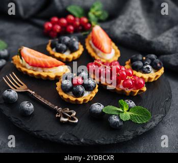 Deliziose tartine con frutta e crema di mascaropne su tavola nera Foto Stock