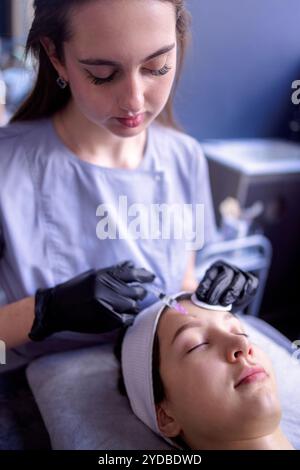 Iniezioni di bellezza. Cosmetologa donna in guanti neri fa un'iniezione Foto Stock