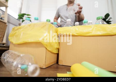 Casa riciclare eco-green zero Concept uomo che lancia bottiglie di plastica vuote in un cestino con sacchetti per rifiuti gialli a casa Foto Stock