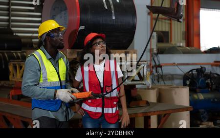 Due tecnici che ispezionano e testano il funzionamento delle gru di sollevamento in impianti industriali pesanti. Foto Stock