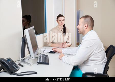 Giovane medico maschile che esamina e consulta giovane paziente femminile in clinica ospedaliera. Consulente professionista di medicina generale Foto Stock