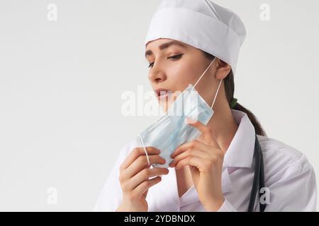 Ritratto di giovane medico femminile indossare la maschera facciale medica protettiva su sfondo bianco, spazio copia Foto Stock