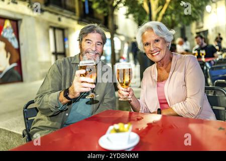 Coppia senior che brinda con la macchina fotografica e goditi la serata in città seduti al bar sul marciapiede Foto Stock
