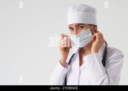 Ritratto di giovane medico femminile indossare la maschera facciale medica protettiva su sfondo bianco, spazio copia Foto Stock