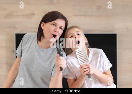 Famiglia felice madre giovane adulta e figlia adolescente carina che si diverte a cantare karaoke con i pennelli. madre ridendo godendo Foto Stock