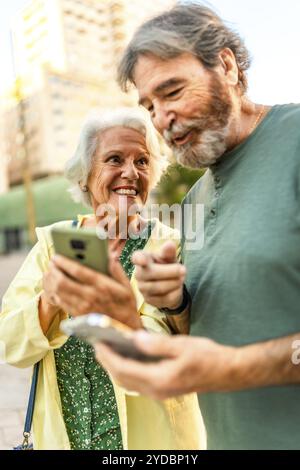 Primo piano verticale di una coppia senior felice che cammina utilizzando il telefono cellulare in città Foto Stock