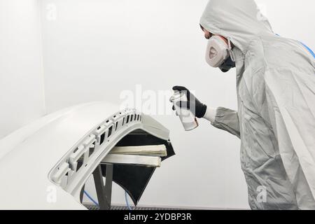 Verniciatura meccanica paraurti di un'auto con irroratrice in cabina di verniciatura in riparazione auto service Foto Stock