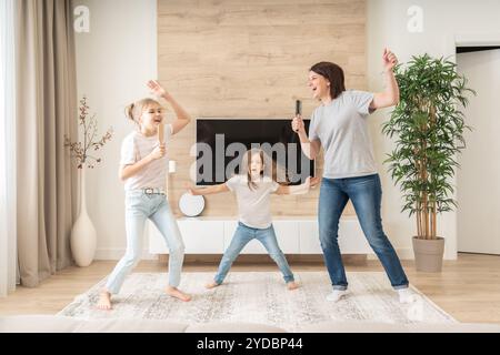 Madre felice e due figlie che si divertono a cantare karaoke con i pennelli. madre ridendo godendo di divertenti attività di stile di vita Foto Stock